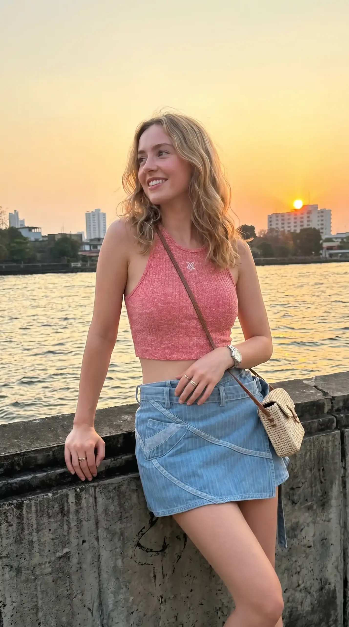 Woman wearing coral pink ribbed halter top with denim mini skirt by the waterfront at sunset
