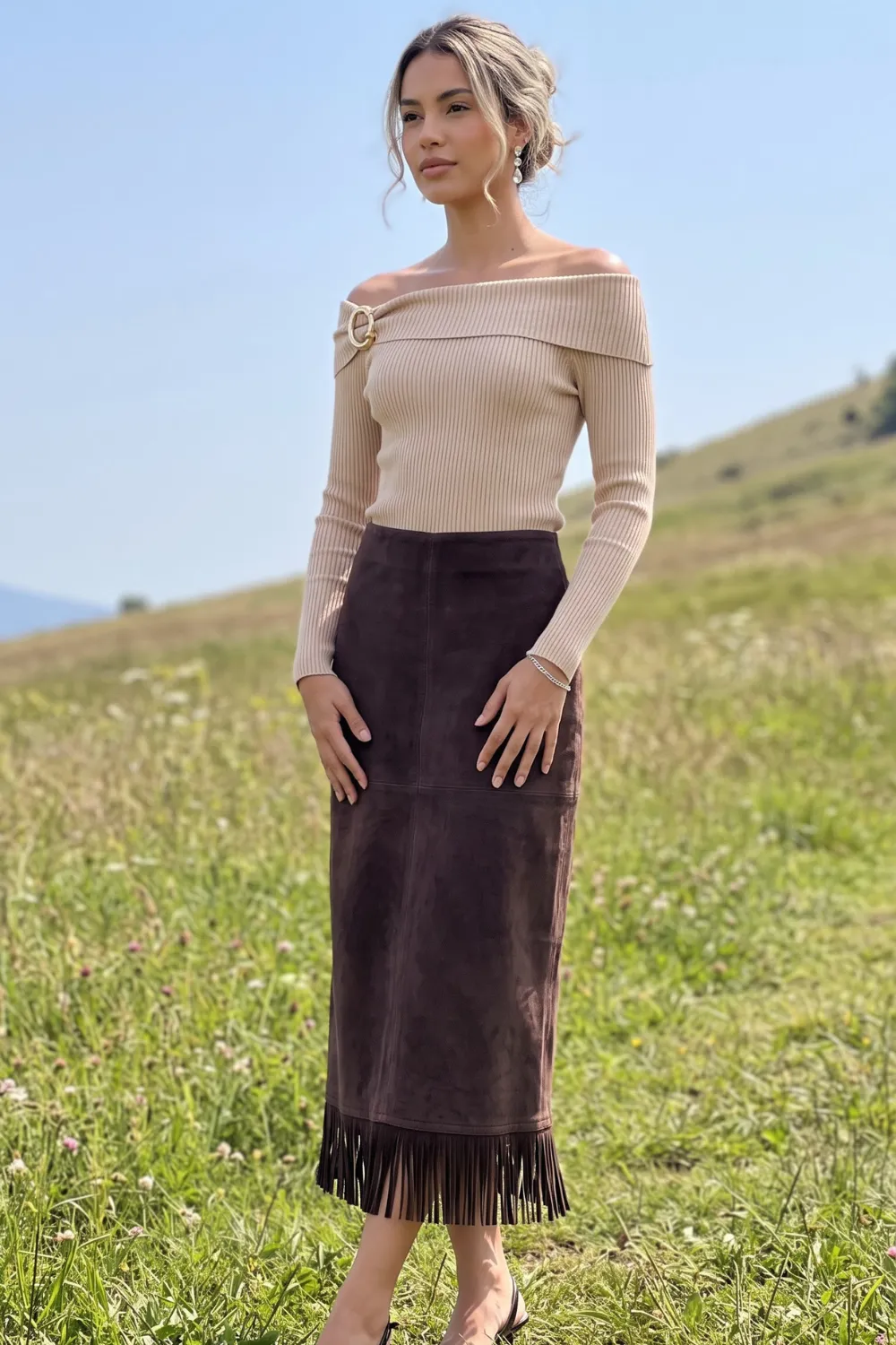 Woman in beige off shoulder gold buckle ribbed knit top and dark brown suede fringe hem midi skirt