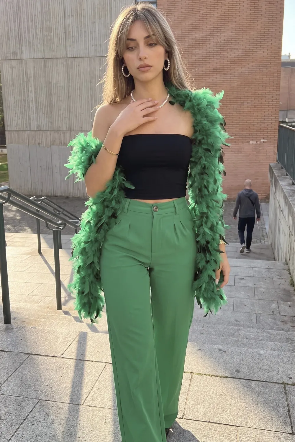 Woman in black bandeau crop top with green wide leg trousers and green feather boa
