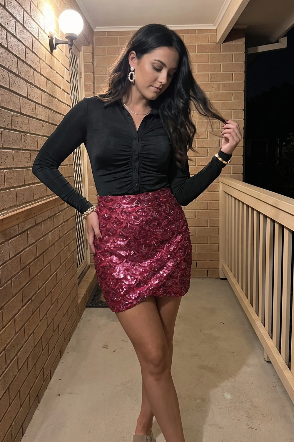 Woman in black ruched long sleeve button shirt with burgundy scallop sequin mini skirt