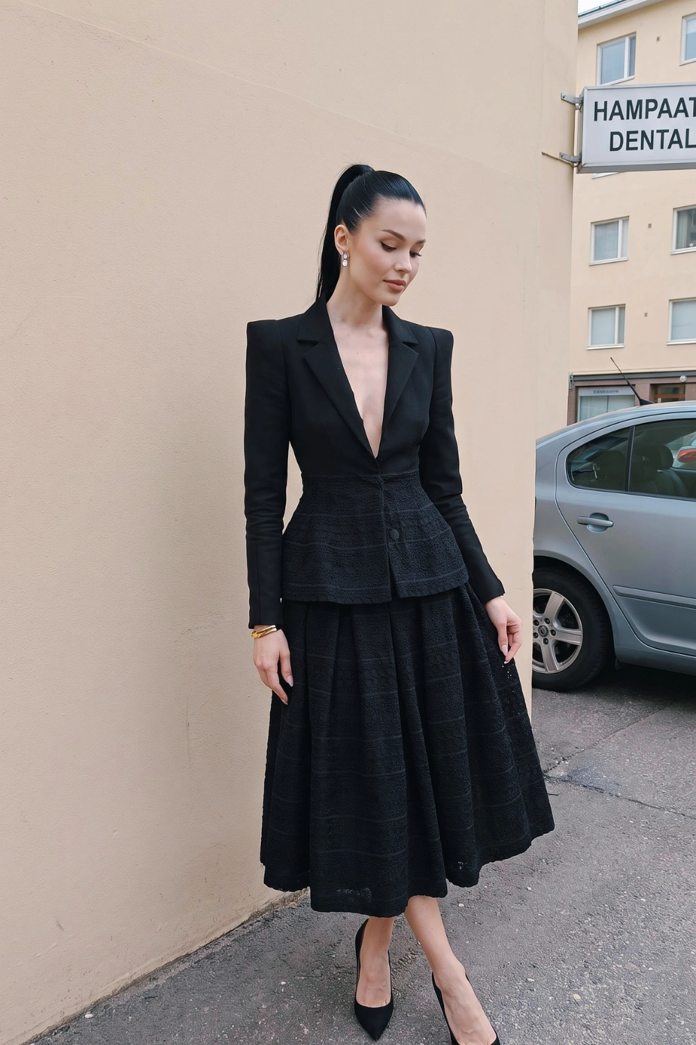 Woman in black deep v structured blazer and black textured pleated midi skirt