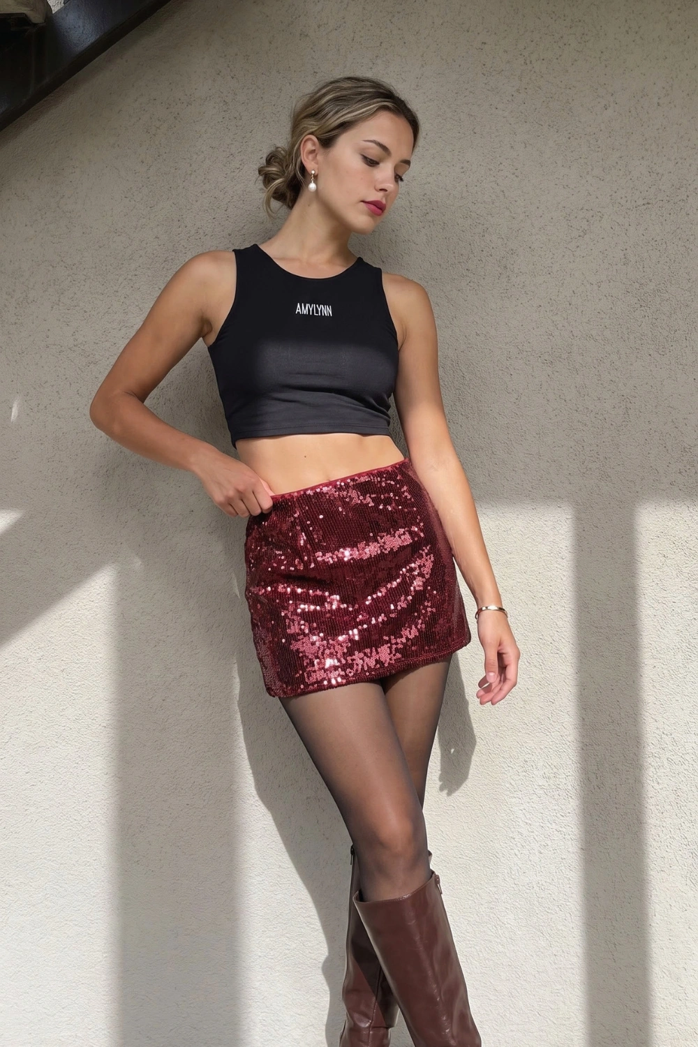 Woman in black crop tank with burgundy sequin mini skirt black tights and dark brown knee high boots