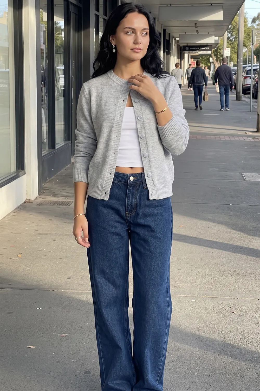 Woman in grey cardigan with white crop top and dark blue wide leg jeans