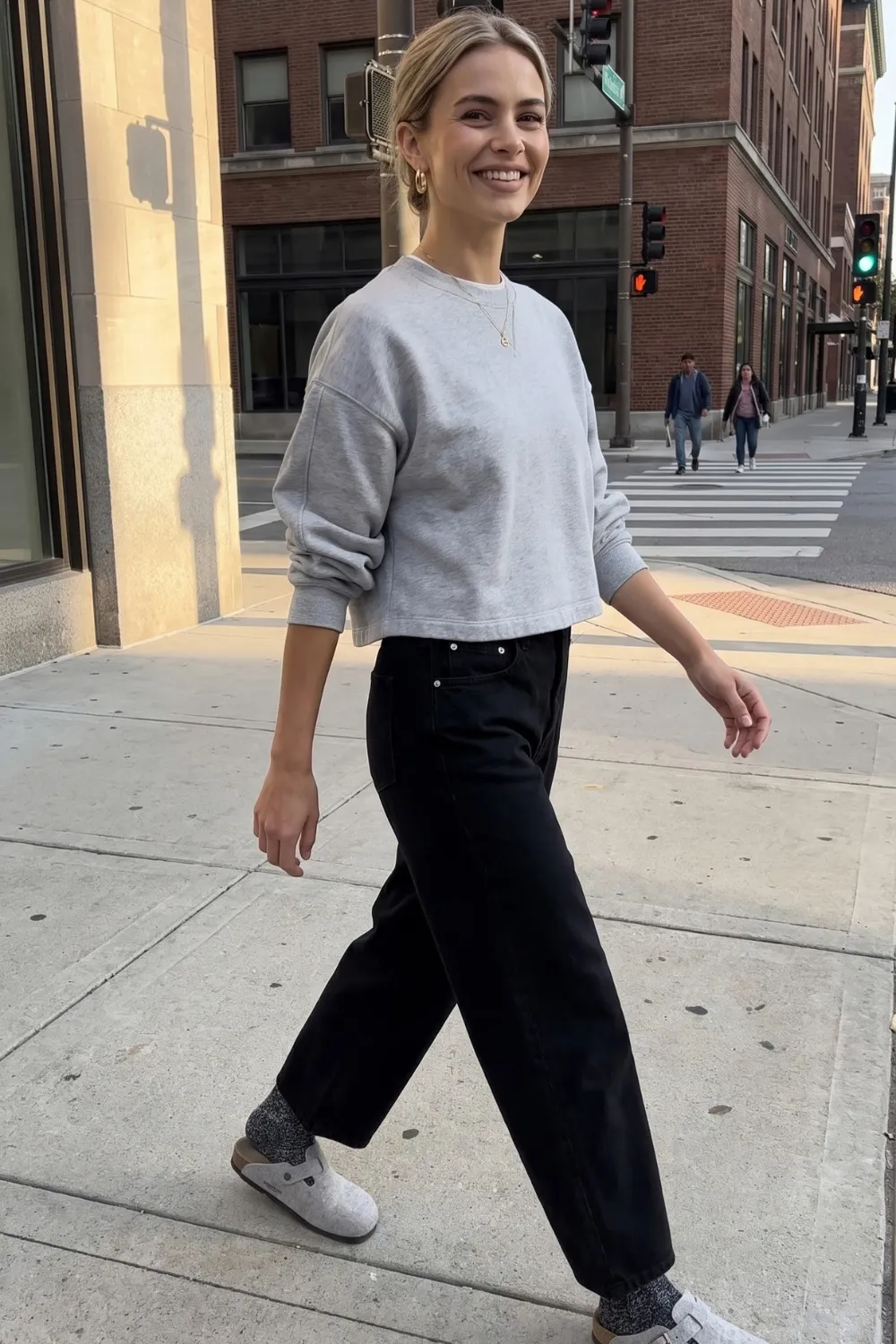 Woman in grey cropped sweatshirt with black barrel jeans and grey clogs