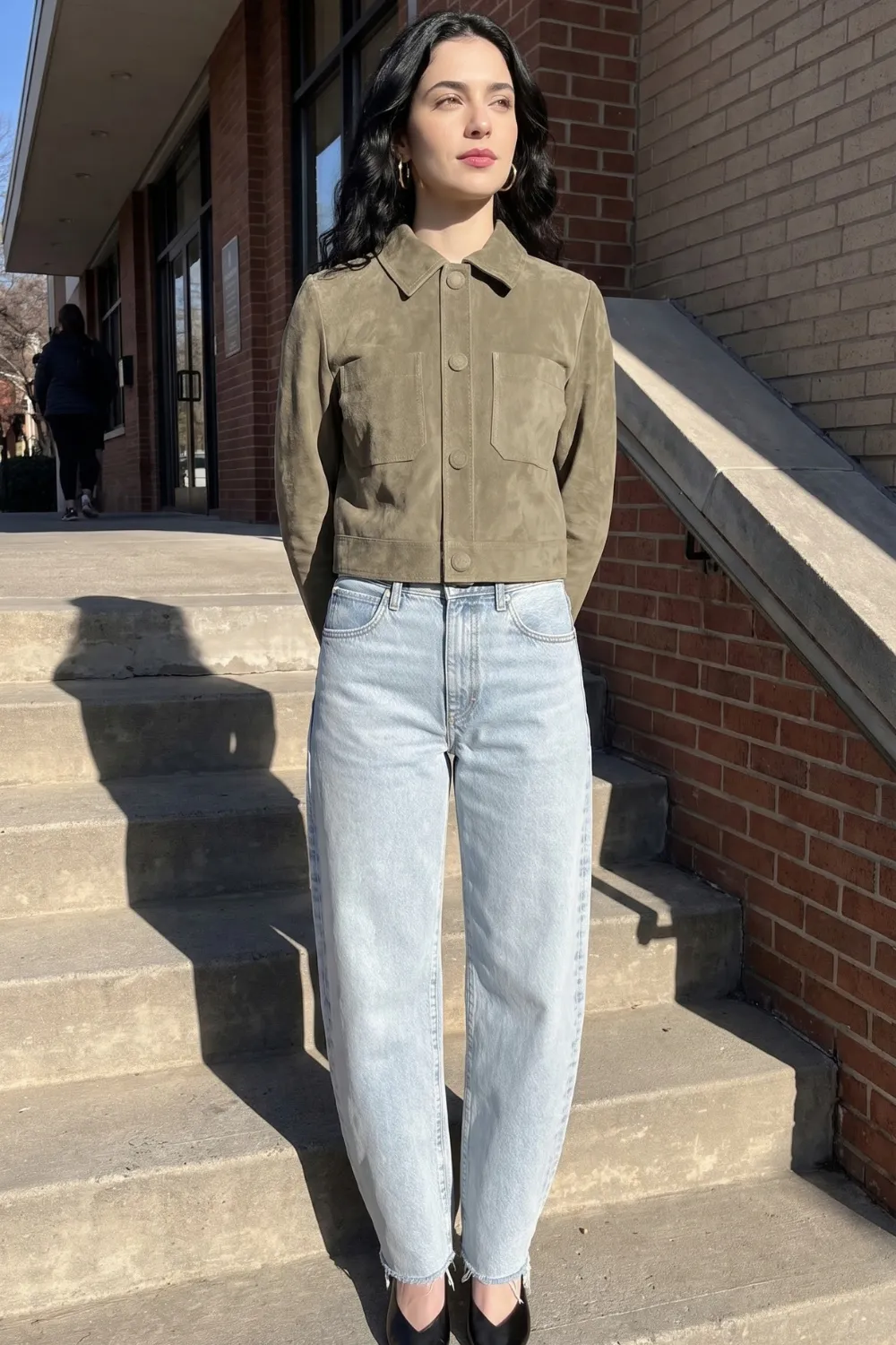 Woman in olive green suede cropped jacket with light wash barrel jeans and black pointed heels