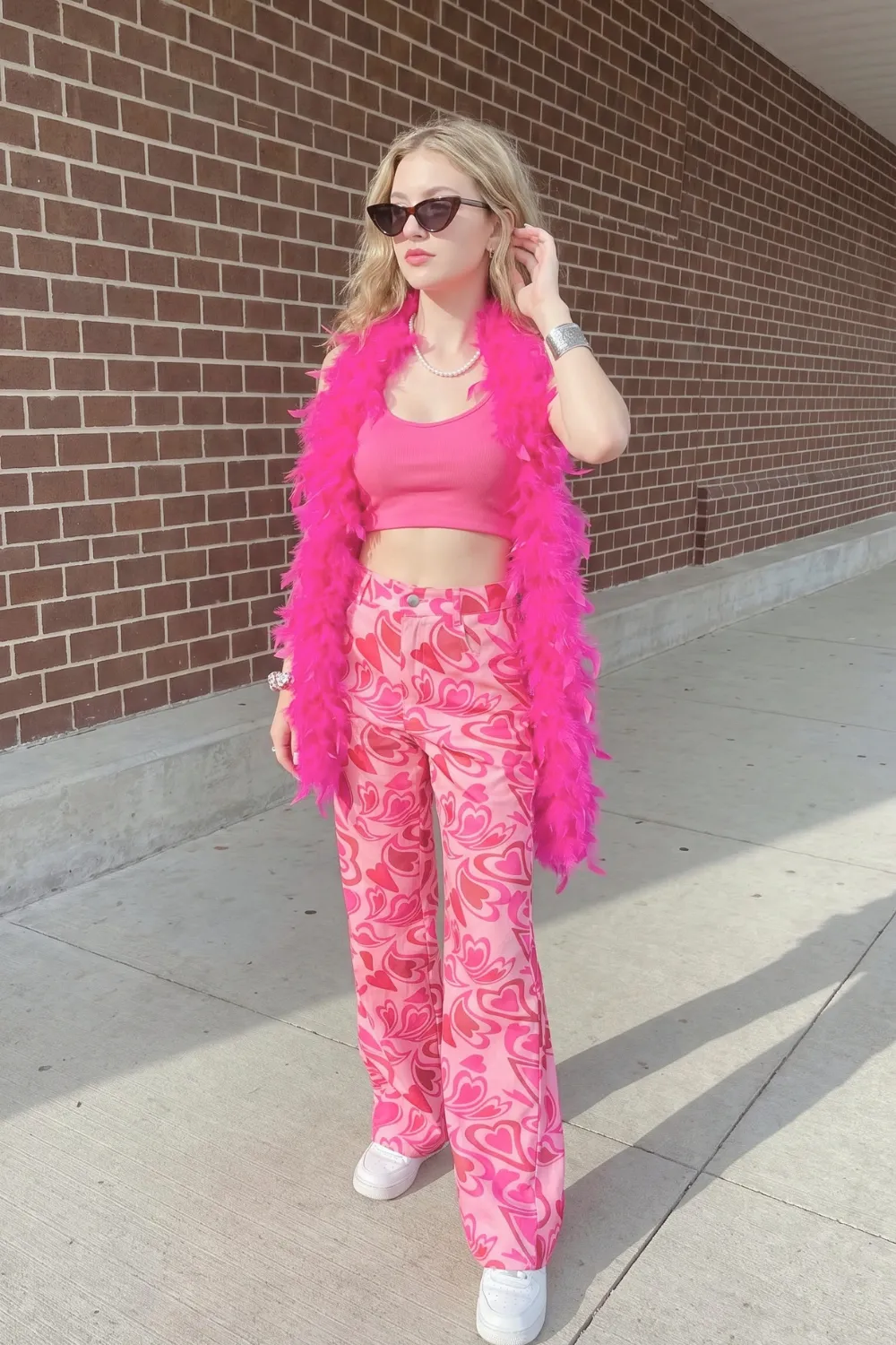 Woman in pink crop tank top with pink red heart print wide leg pants and hot pink feather boa