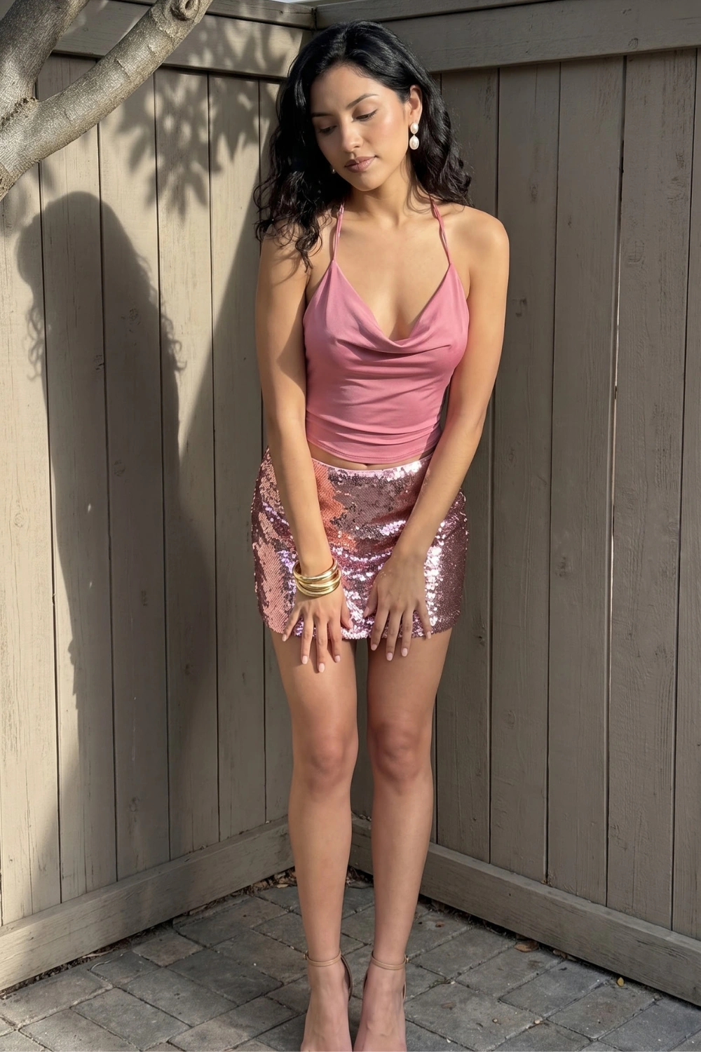Woman in pink cowl neck halter top with rose gold pink sequin mini skirt and nude strappy heels