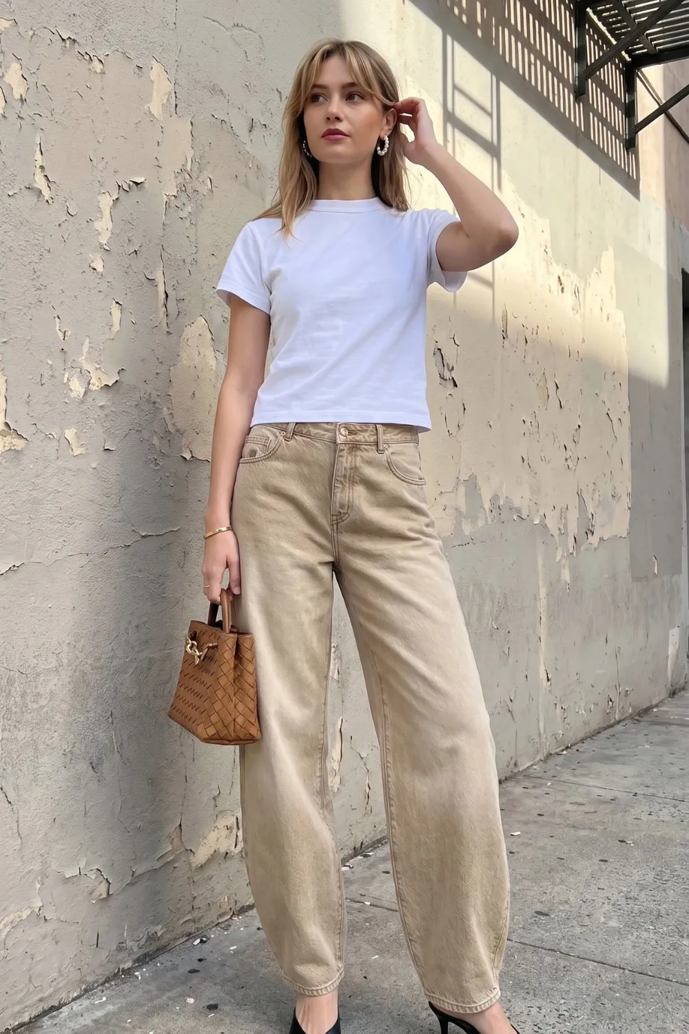 Woman in white fitted crew neck tee with sand beige washed barrel jeans and black pointed heels