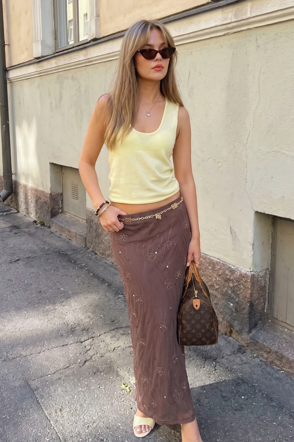 Woman in pale yellow sleeveless tank top and brown embellished sequin mesh maxi skirt with gold chain belt